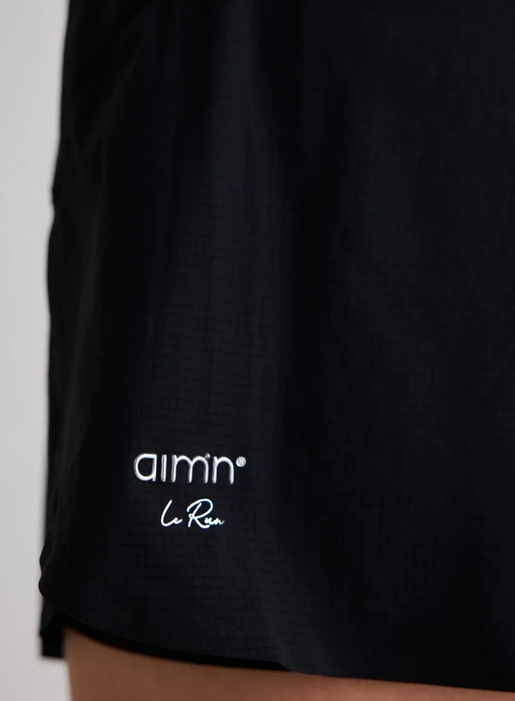 Detail van het aim'n logo en de ademende stof van de zwarte running shorts