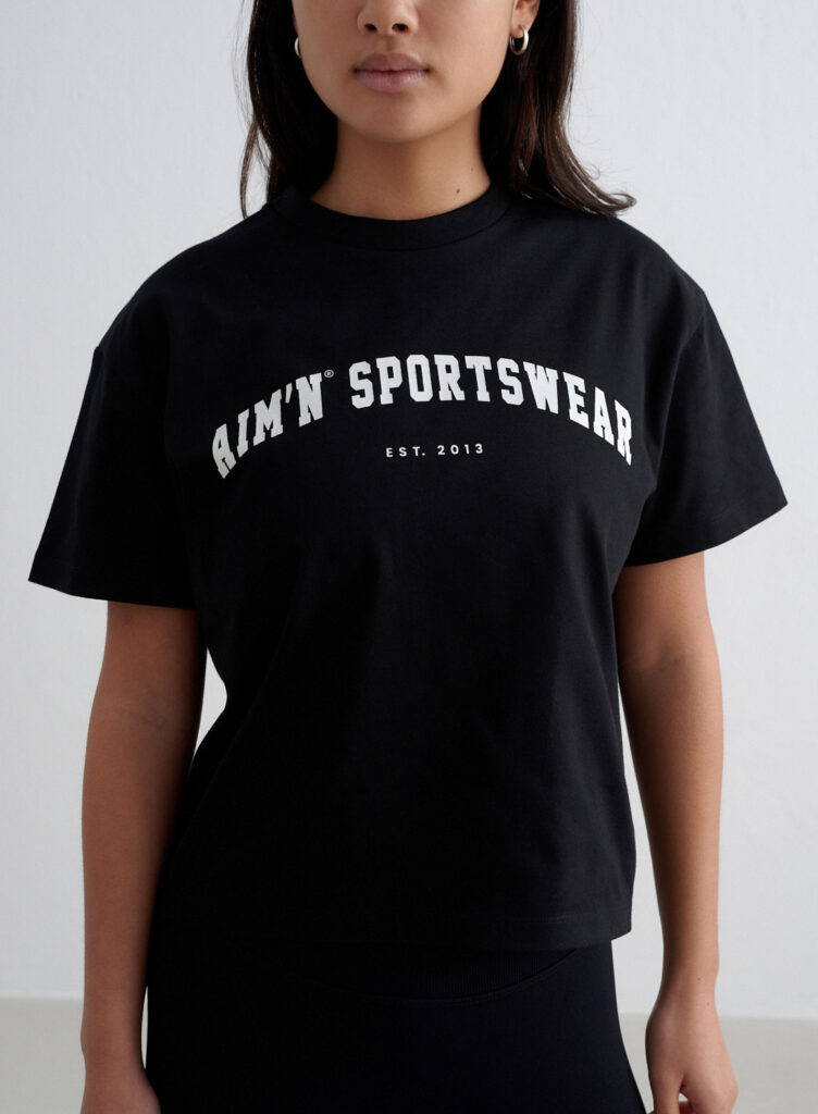 Aim'n Black Varsity Boxy T-shirt 24080607-010 dames shirt in het zwart met Varsity logo en boxy pasvorm