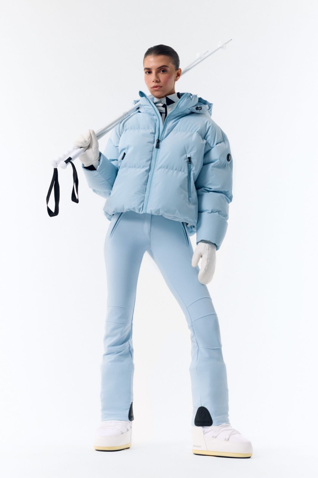 Vrouw in lichtblauwe Airforce Sport ski-jas en skibroek met skistokken